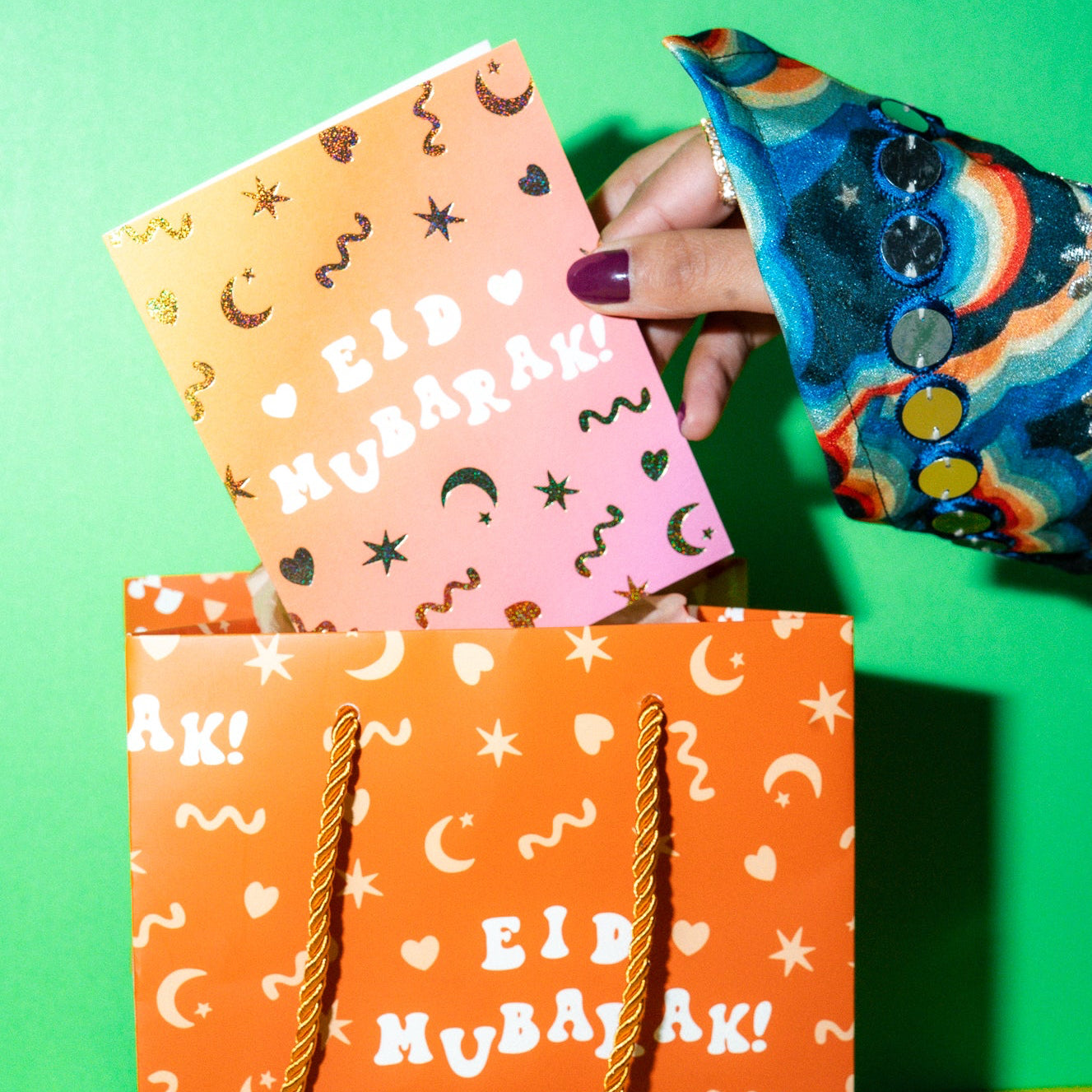 Orange 'Eid Mubarak!' gift bag with colorful cards on a green background