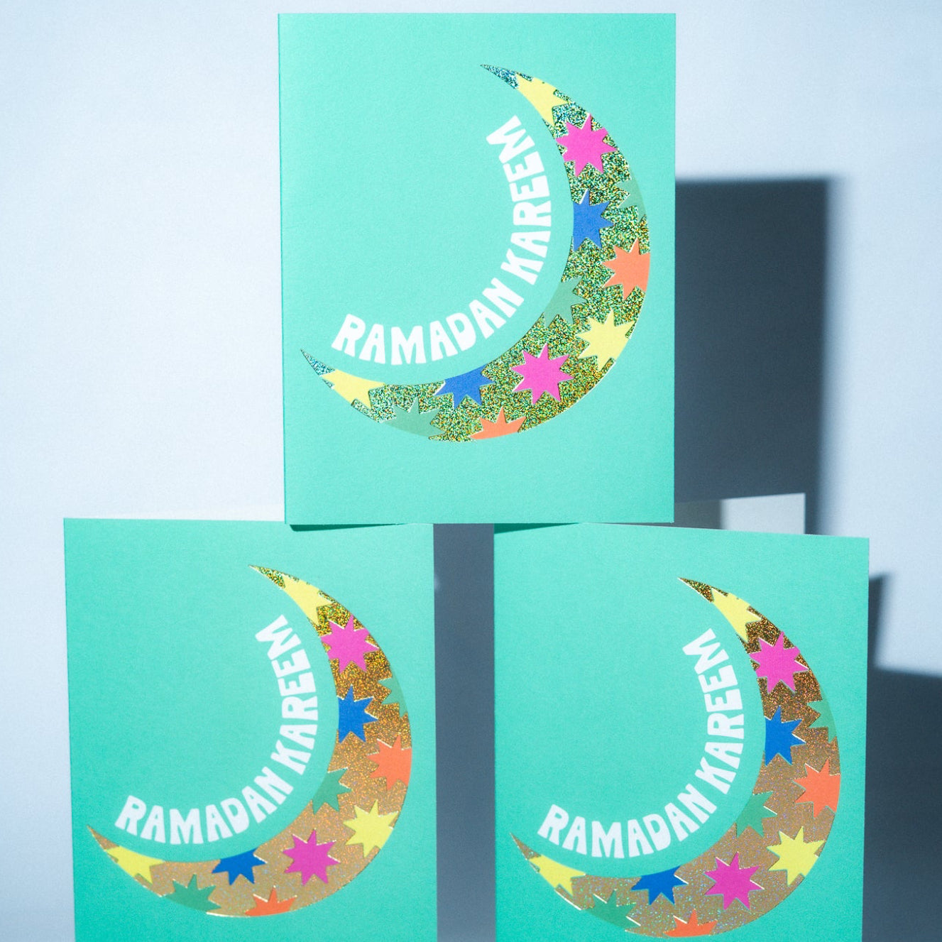 Three teal cards with colorful crescent moon designs and 'Ramadan Kareem' text on a light blue background.