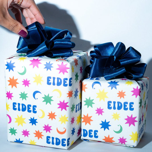 Two gift boxes with colorful star-patterned paper and blue ribbons, one being held by a hand.