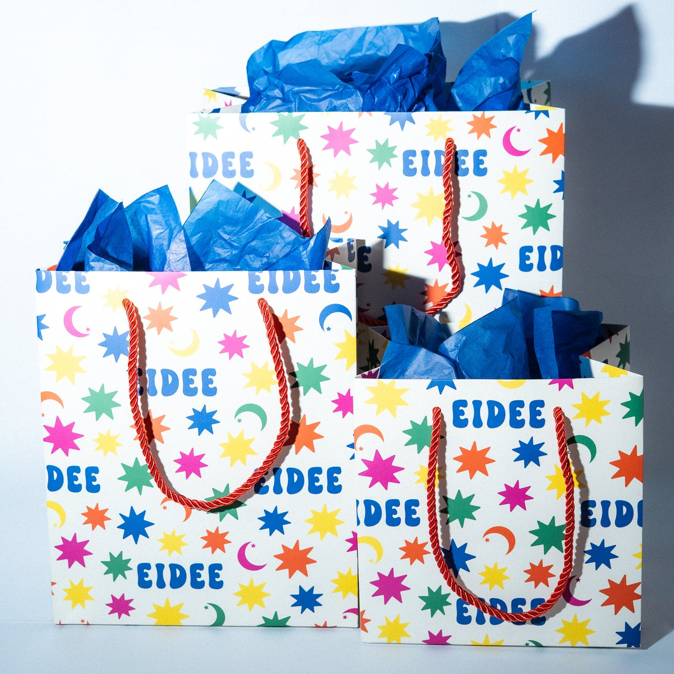 Two colorful gift bags with blue tissue paper on a light blue background